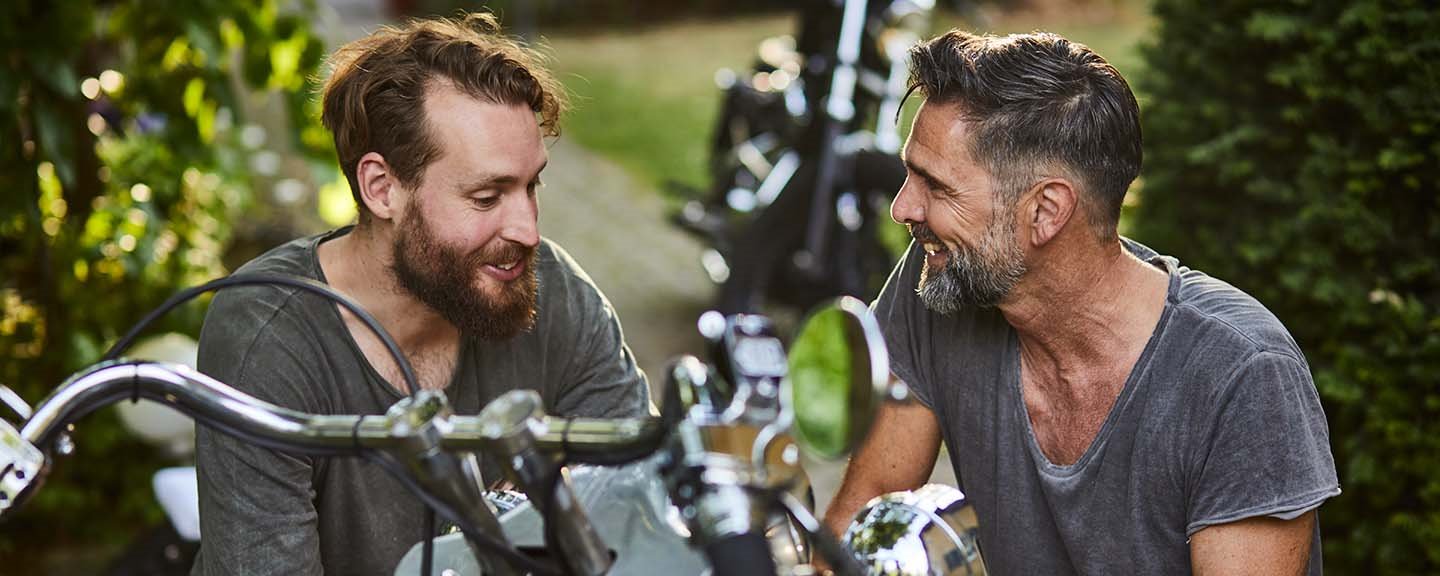 Två män mekar med motorcykel i trädgården