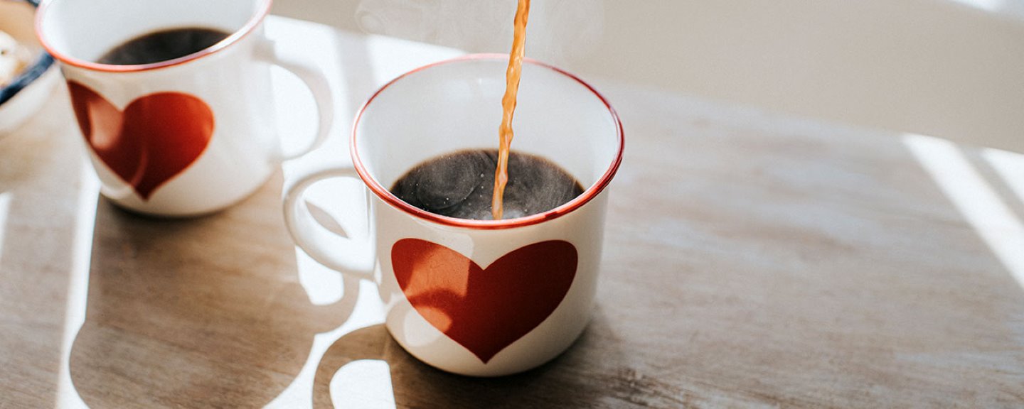 Varmt kaffe hälls upp i två vita kaffekoppar med rött hjärta på