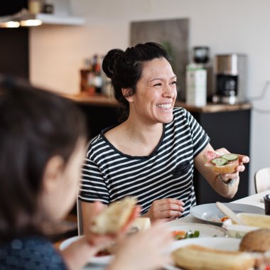 Leende mamma sitter vid köksbordet och äter frukost med sin dotter