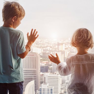 Pojke och flicka tittar ut över storstad vid panoramafönster på hotellrum