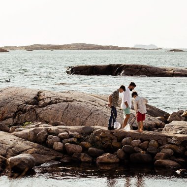 Pappa och söner på klipphällar vid havet håller fiskehåvar